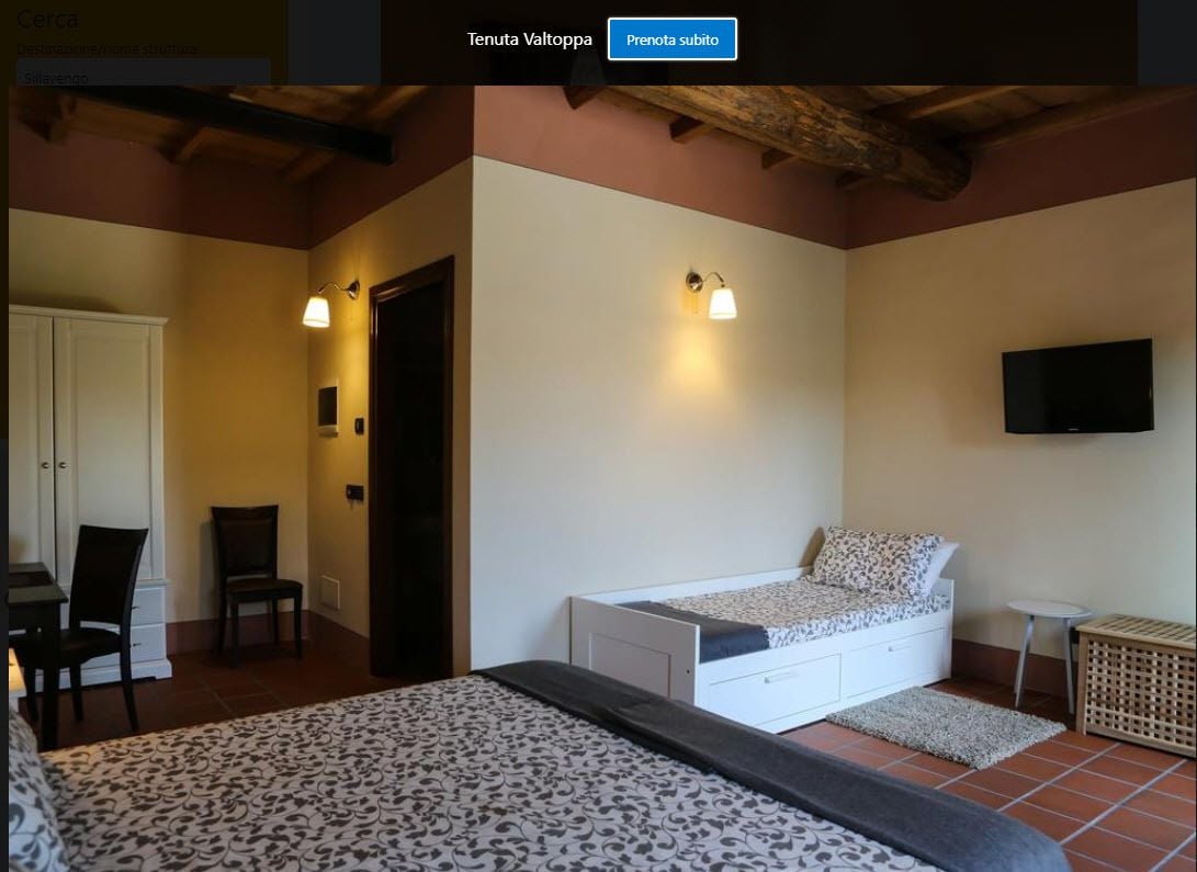 A bedroom with a bed, a desk, two chairs, a television, and a small table.