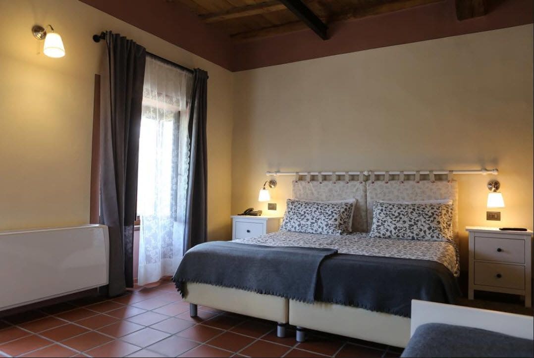 A bedroom with a bed, bedside tables, a lamp, a radiator, and a window with curtains.