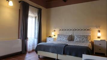 A bedroom with a bed, bedside tables, a lamp, a radiator, and a window with curtains.
