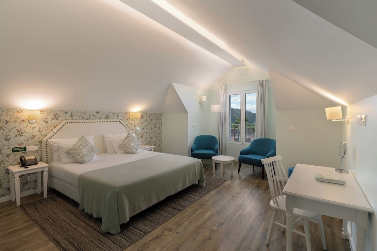 A bedroom with a bed, two chairs, a desk, and a window with curtains.