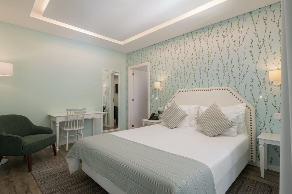 A bedroom with a bed, a desk, a chair, and a mirror.