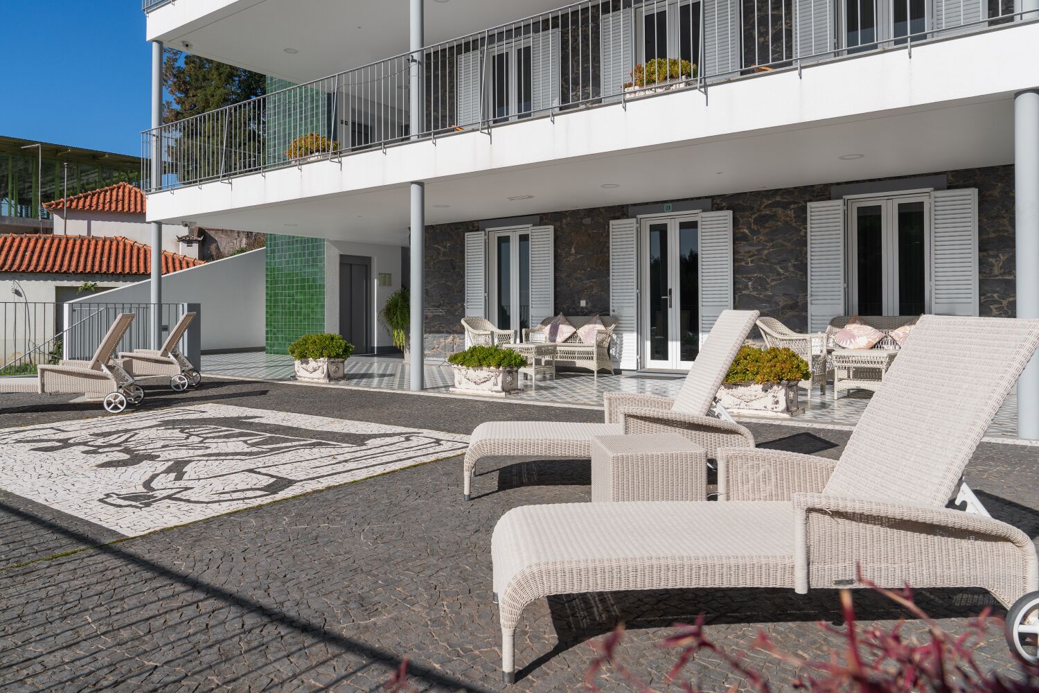 Un edificio moderno con balcón, zona de estar exterior y un patio empedrado.