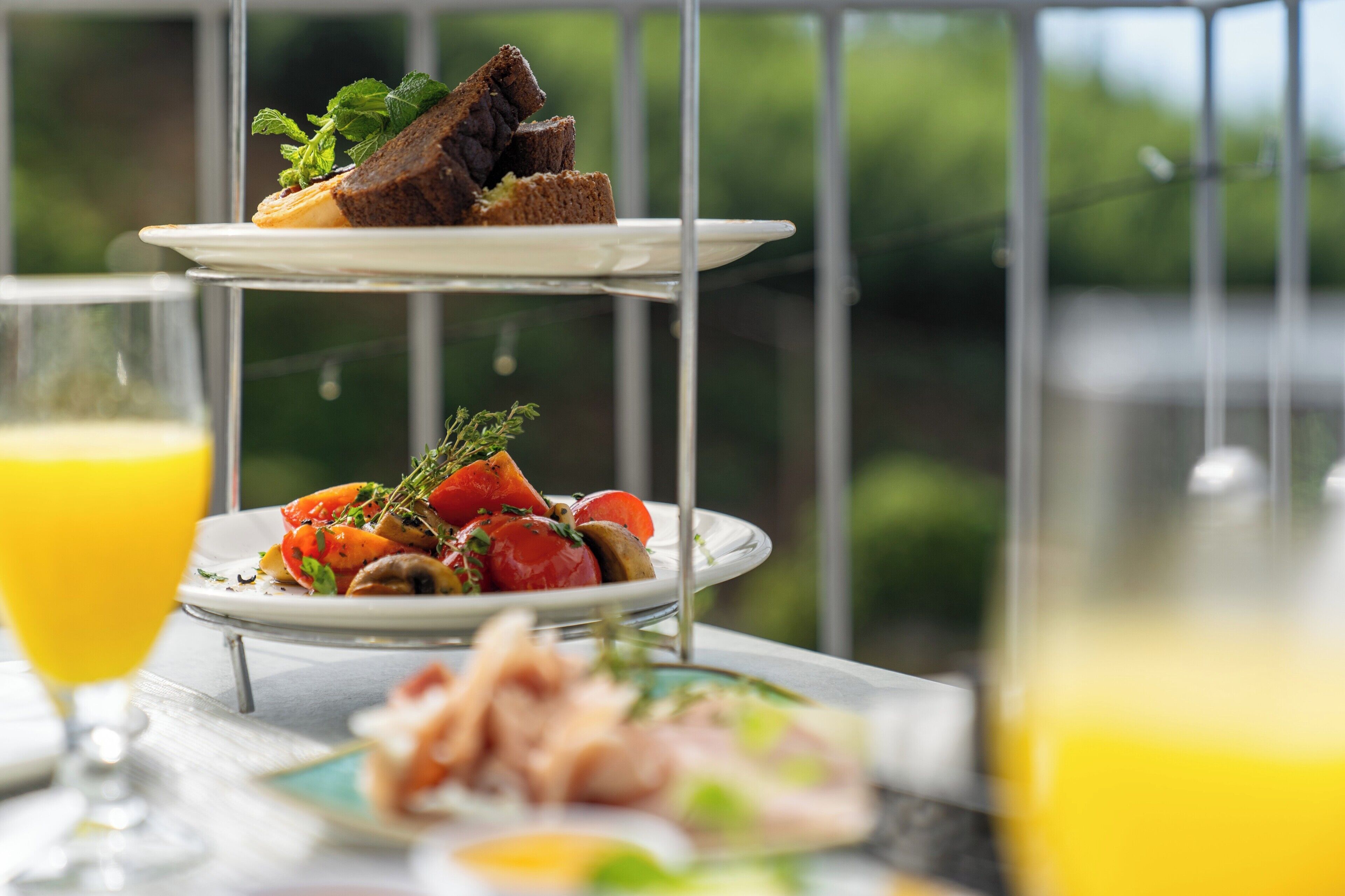 A dining table with a two-tiered serving tray, a glass of orange juice, and plates of food.