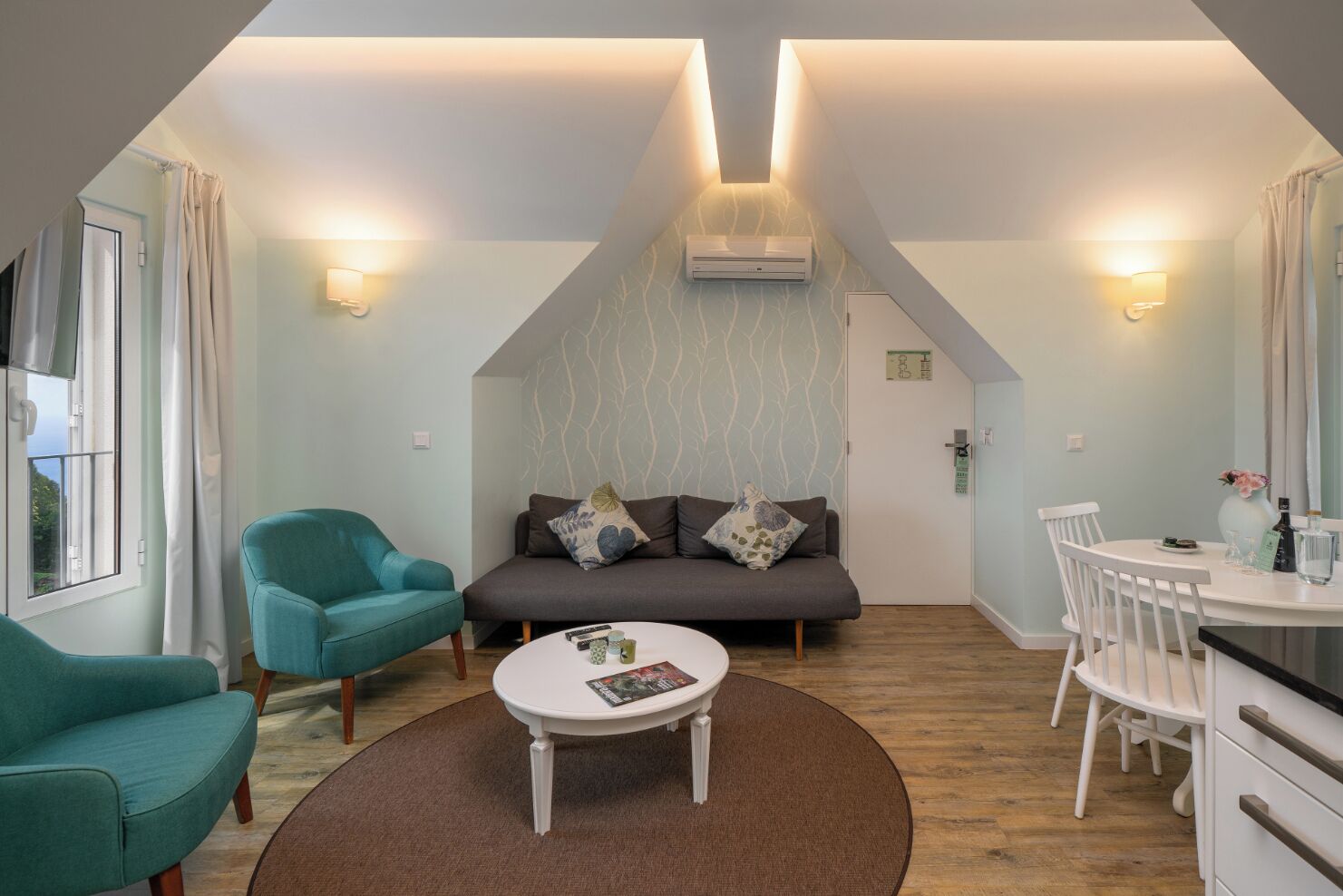 A cozy loft-style room with a sofa, two chairs, a dining table, and a small round table with a magazine.