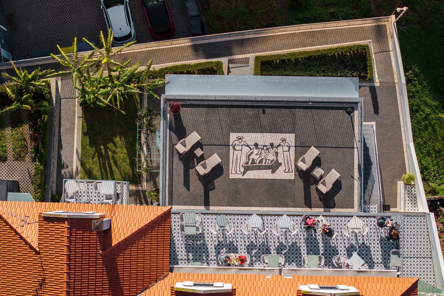 An aerial view of a rooftop terrace with seating areas, a decorative mural, and a small garden.