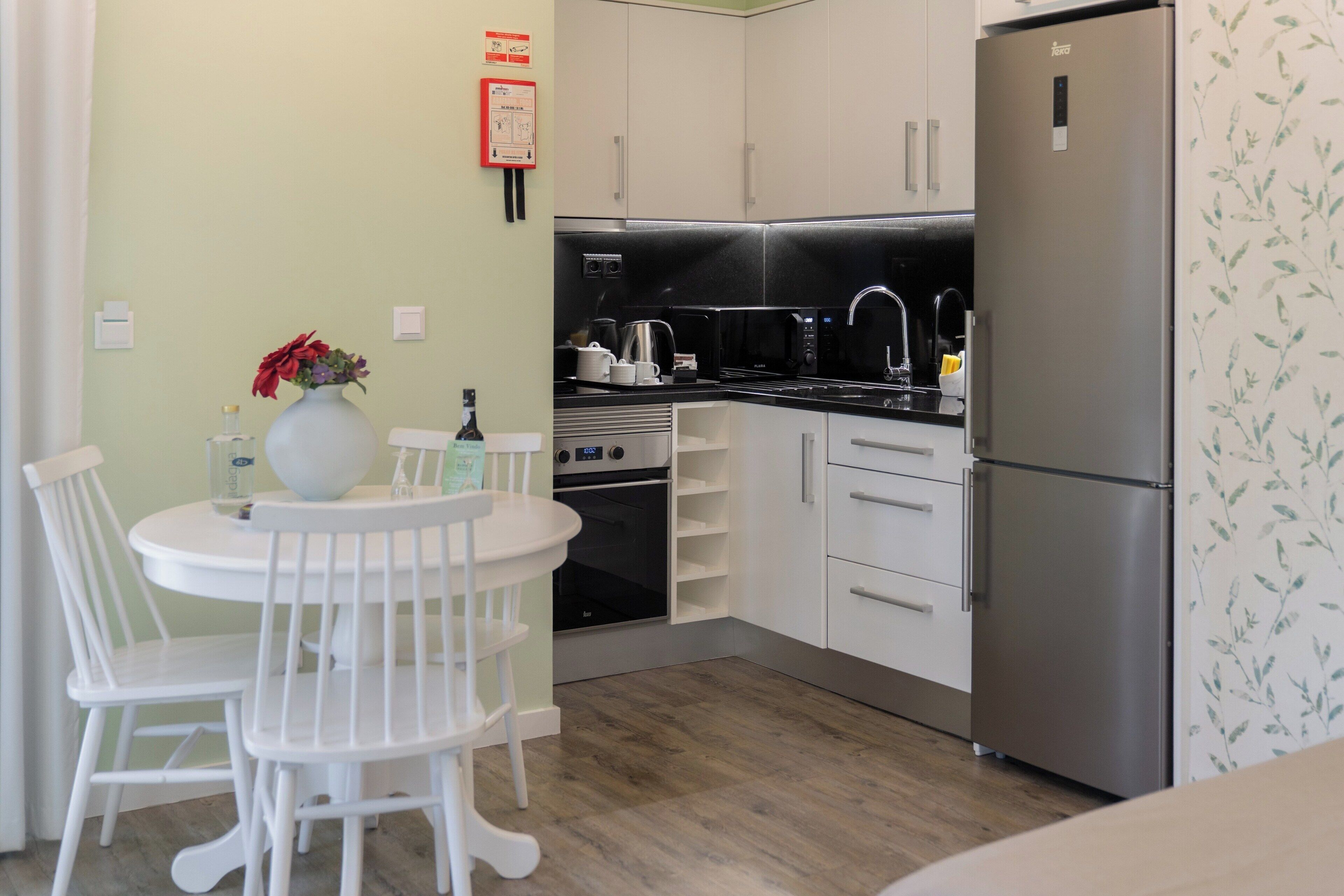 A compact kitchen with white cabinets, a stainless steel refrigerator, a microwave, and a stove. There is a white table with chairs and a vase with flowers.