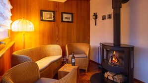 Una habitación acogedora con suelo de madera, mobiliario de mimbre, una mesa con una copa de vino y un estufa de leña.