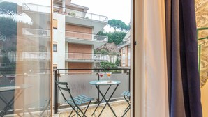 Ein Balkon mit Tisch und Stühlen, ein kleiner Tisch mit Getränken und Blick auf ein Gebäude mit mehreren Balkonen.