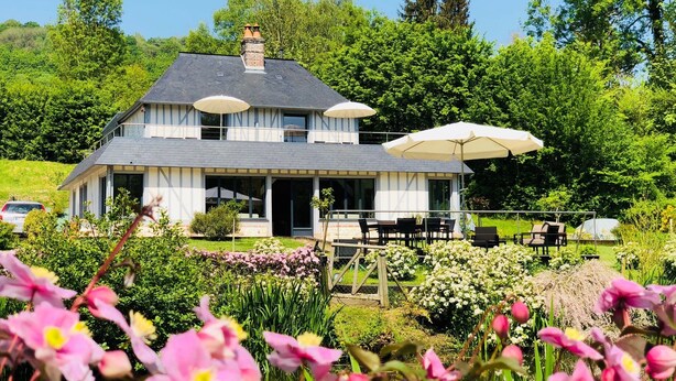 Een herenhuis met balkon, omgeven door weelderige begroeiing en bloeiende planten.