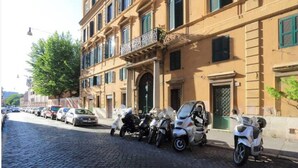 Rua de paralelepípedos com carros e motocicletas estacionados.