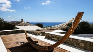 Una hamaca en una terraza de madera con vistas panorámicas al mar y a la costa lejana.