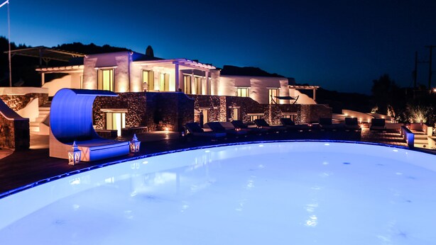 Un hotel moderno con piscina, sillas de descanso y fachada de piedra.