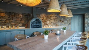 Una larga mesa de madera con sillas de mimbre, una pared de piedra y una chimenea de piedra.