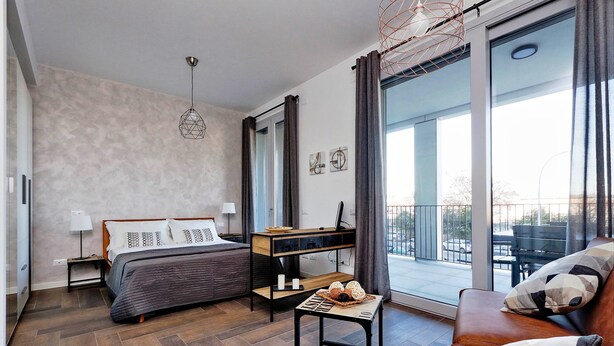 Un dormitorio moderno con cama, escritorio, sofá y balcón con vistas.