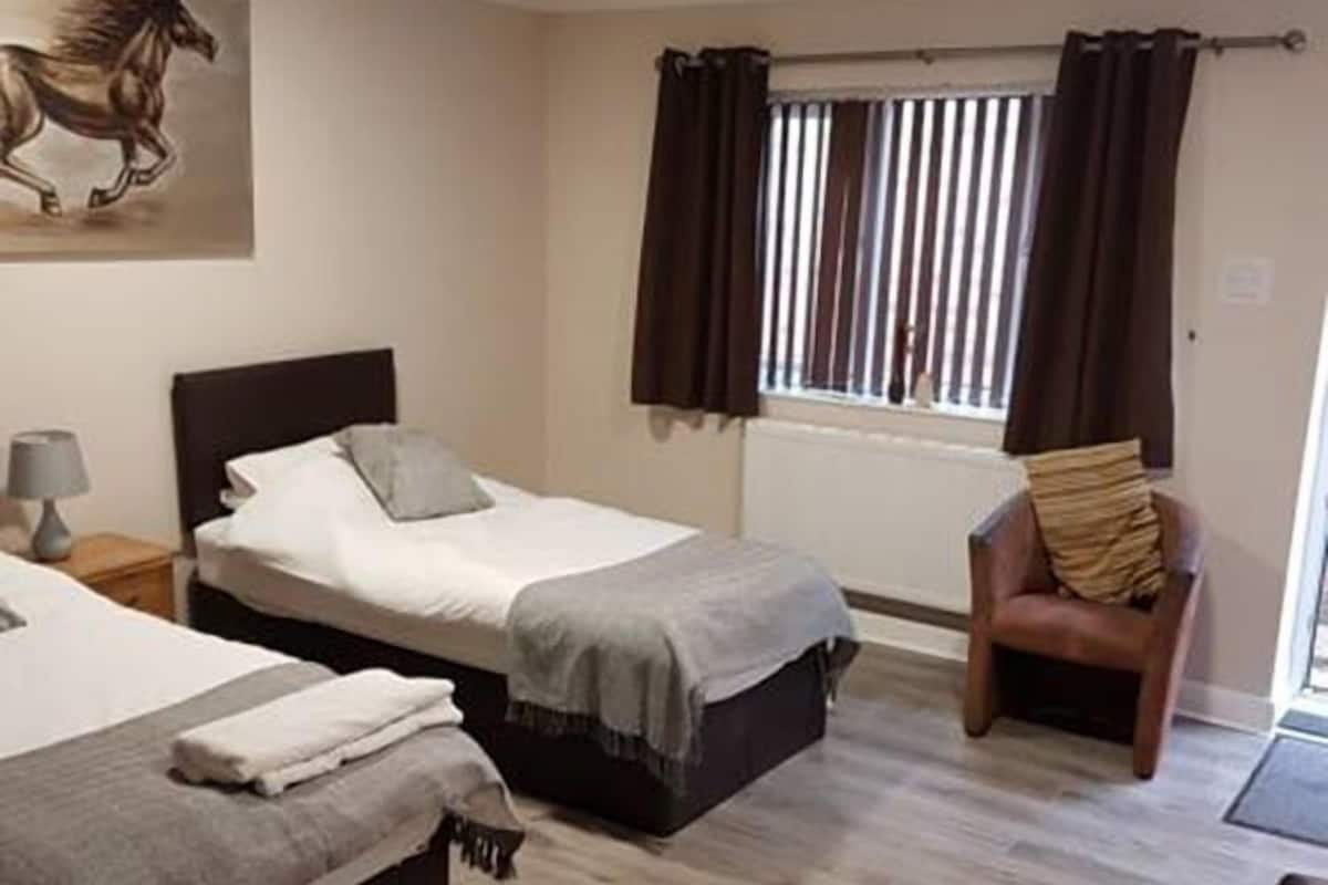 Quarto de hotel com duas camas, uma cadeira, um quadro e uma janela com cortinas.