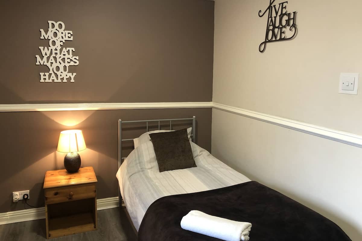 Quarto com cama, mesa de cabeceira com abajur e arte decorativa na parede.