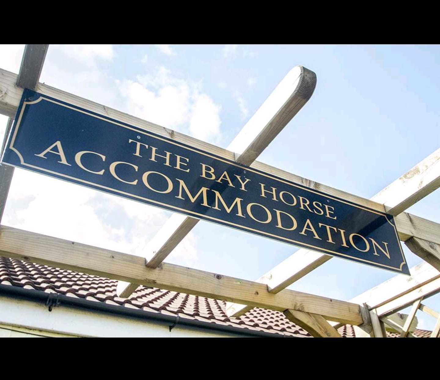 A sign for "The Bay Horse Accommodation" with a clear view of the sky and part of a building's roof.