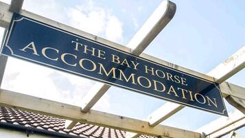 A sign for "The Bay Horse Accommodation" with a clear view of the sky and part of a building's roof.
