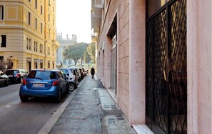 A narrow street with parked cars and buildings on either side.