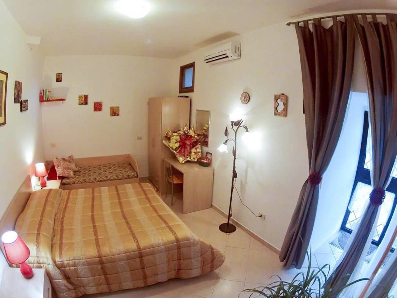 A bedroom with two beds, a desk, a chair, a floor lamp, and a window with curtains.