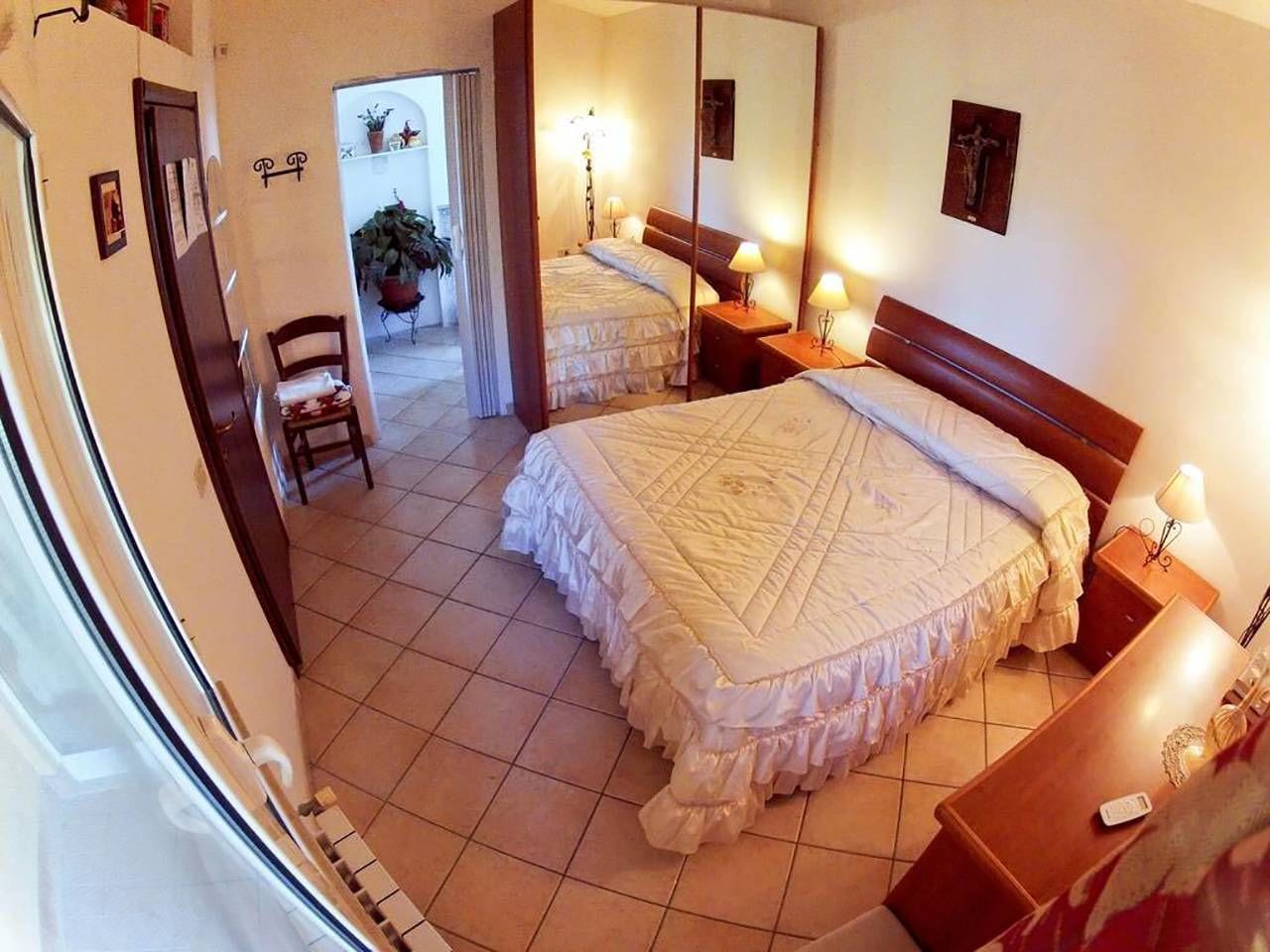 A hotel room with a large bed, a bedside table with a lamp, a chair, and a small table with a remote control.