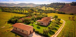 An aerial view of a rural property with multiple buildings, surrounded by green fields and trees, with a hilly landscape in the background. - B&B Le Cascatelle (Cerveteri)