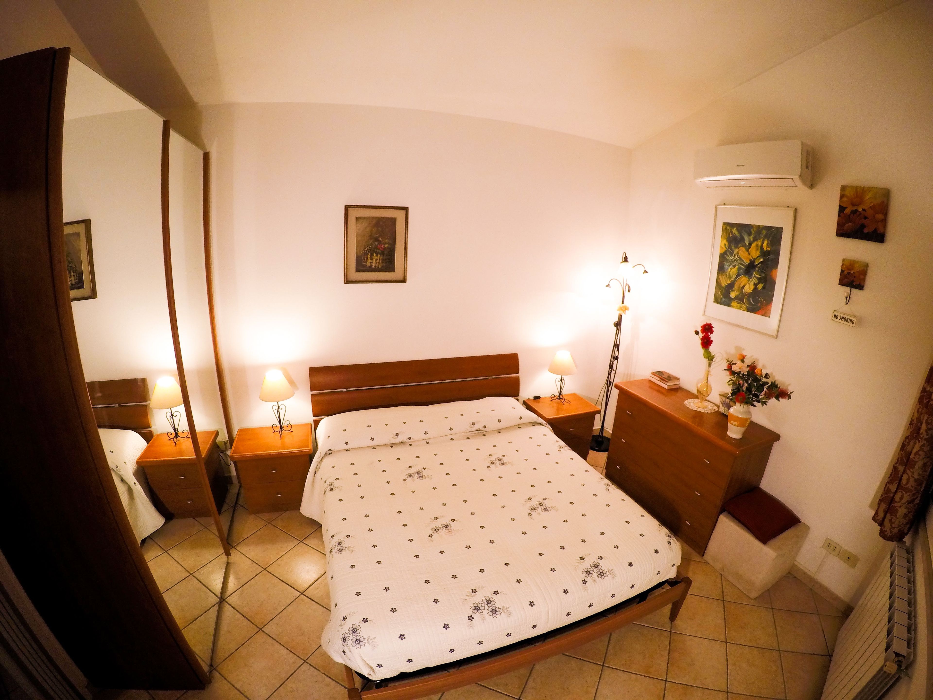 A bedroom with a bed, bedside tables, a nightstand, a dresser, a mirror, and a radiator.