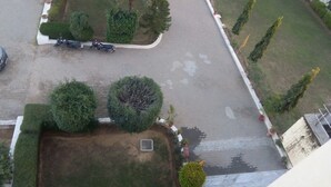 An aerial view of a parking area with several motorcycles, a small garden with neatly trimmed bushes, and a paved pathway.
