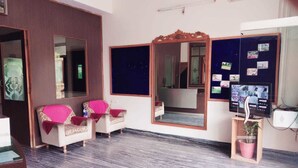 A room with a marble floor, two armchairs with pink cushions, a large mirror, and a wall with photos.