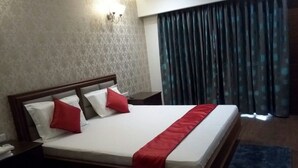 A neatly made bed with a red bedspread and pillows, a nightstand with a lamp, and a window with curtains.