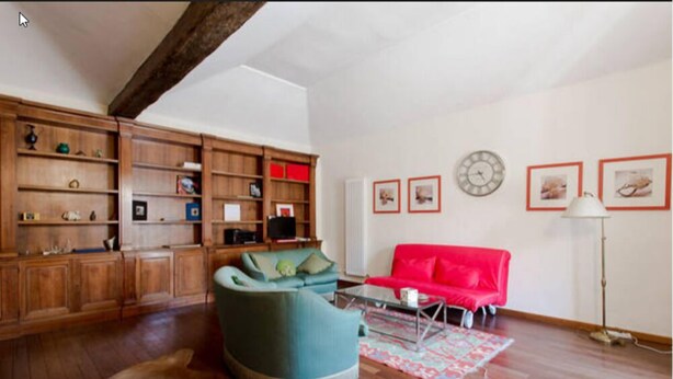 A living room with wooden shelving, a red sofa, a green armchair, and a patterned rug. - Superbe penthouse to Piazza Navona (Rome)