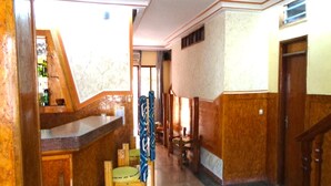 A hotel lobby with a reception desk, wooden chairs, a staircase, and a tiled floor. - Résidence Bonté Divine (Abidjan)
