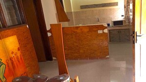 A dining area with a wooden table and chairs, a kitchen in the background, and a view of the outside. - Résidence Bonté Divine (Abidjan)