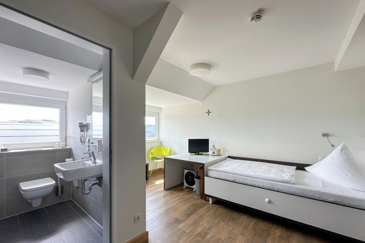 A modern bedroom with a bed, a bedside table, a TV, and a window.