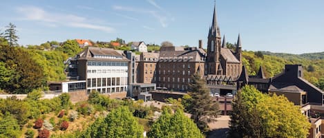 A historic building with a prominent tower, surrounded by lush greenery and modern structures.