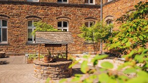 Un patio con un pozo de piedra, un sendero de ladrillo y un edificio de piedra con ventanas arqueadas.