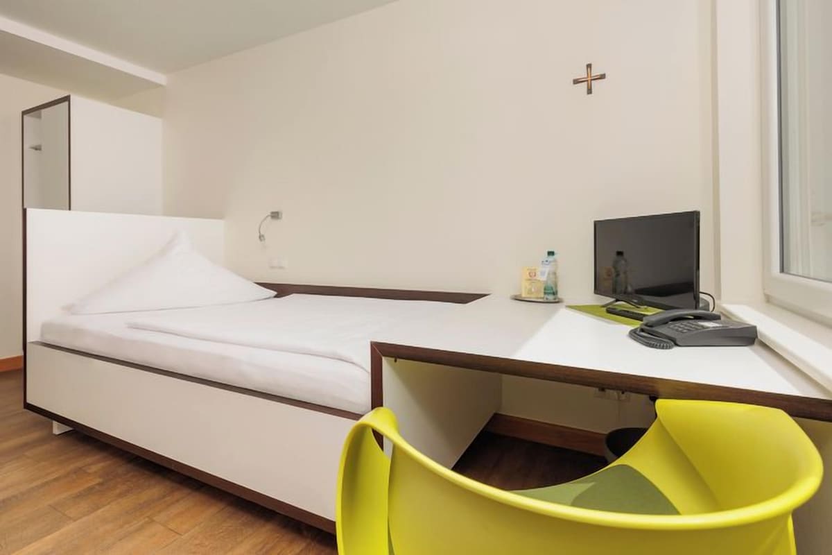 A compact room with a bed, a desk with a computer, and a chair.