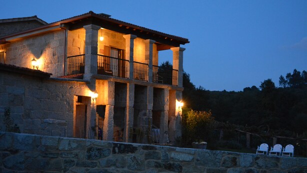 A stone building with a balcony and two lit windows. - Alojamiento Rural Pazos (San Cristovo de Cea)