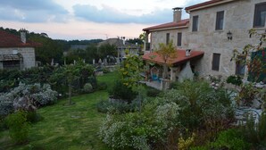 A stone building with a red roof, surrounded by a well-maintained garden with various plants and flowers. - Alojamiento Rural Pazos (San Cristovo de Cea)