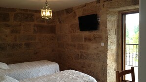A bedroom with two beds, a stone wall, a television mounted on the wall, and a wooden chair. - Alojamiento Rural Pazos (San Cristovo de Cea)