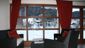 A room with a large window, wicker furniture, and a view of a snowy landscape. - Hotel zum Postillion (Reit im Winkl)
