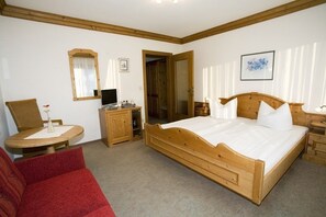 A bedroom with a wooden bed, a red sofa, a small round table with a lamp, and a mirror on the wall.