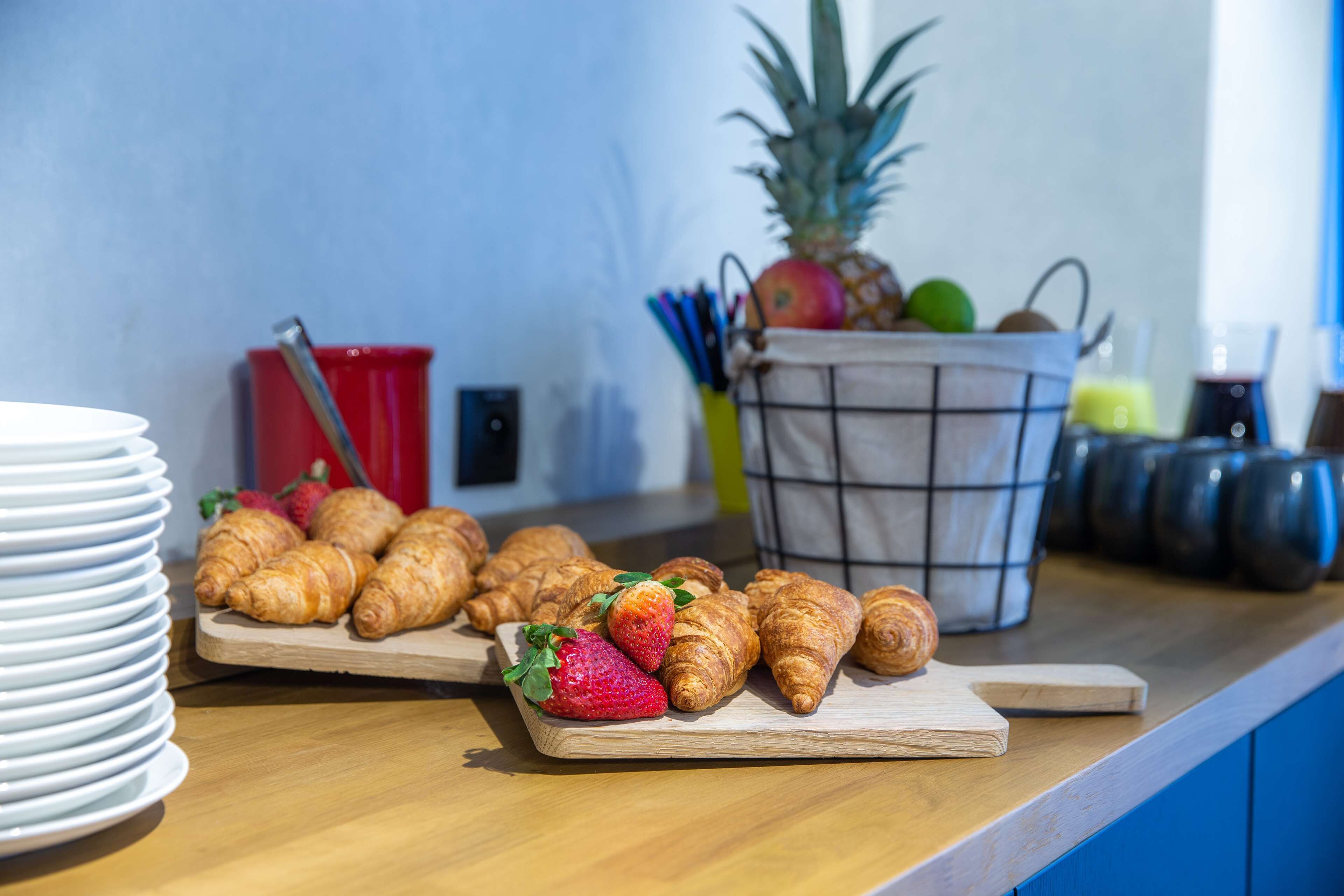 Un bufé de desayuno con croissants, fresas y una piña sobre una tabla de madera.