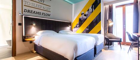A modern hotel room with a large bed, a desk, and a chair. There is a wall with a motivational quote and a large poster.