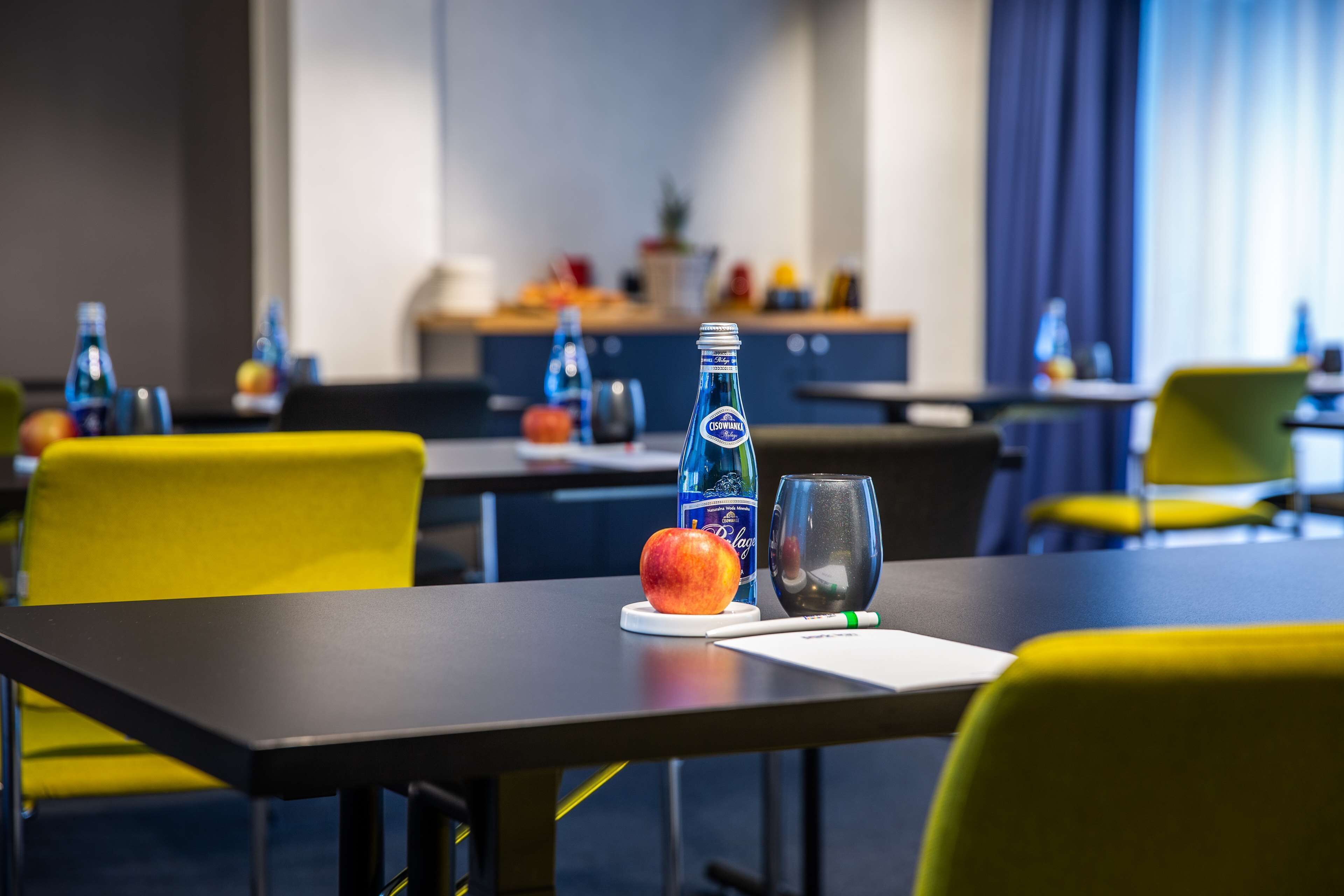 A hotel room with a dining table set with a bottle of water, a glass, a fruit, and a notepad.