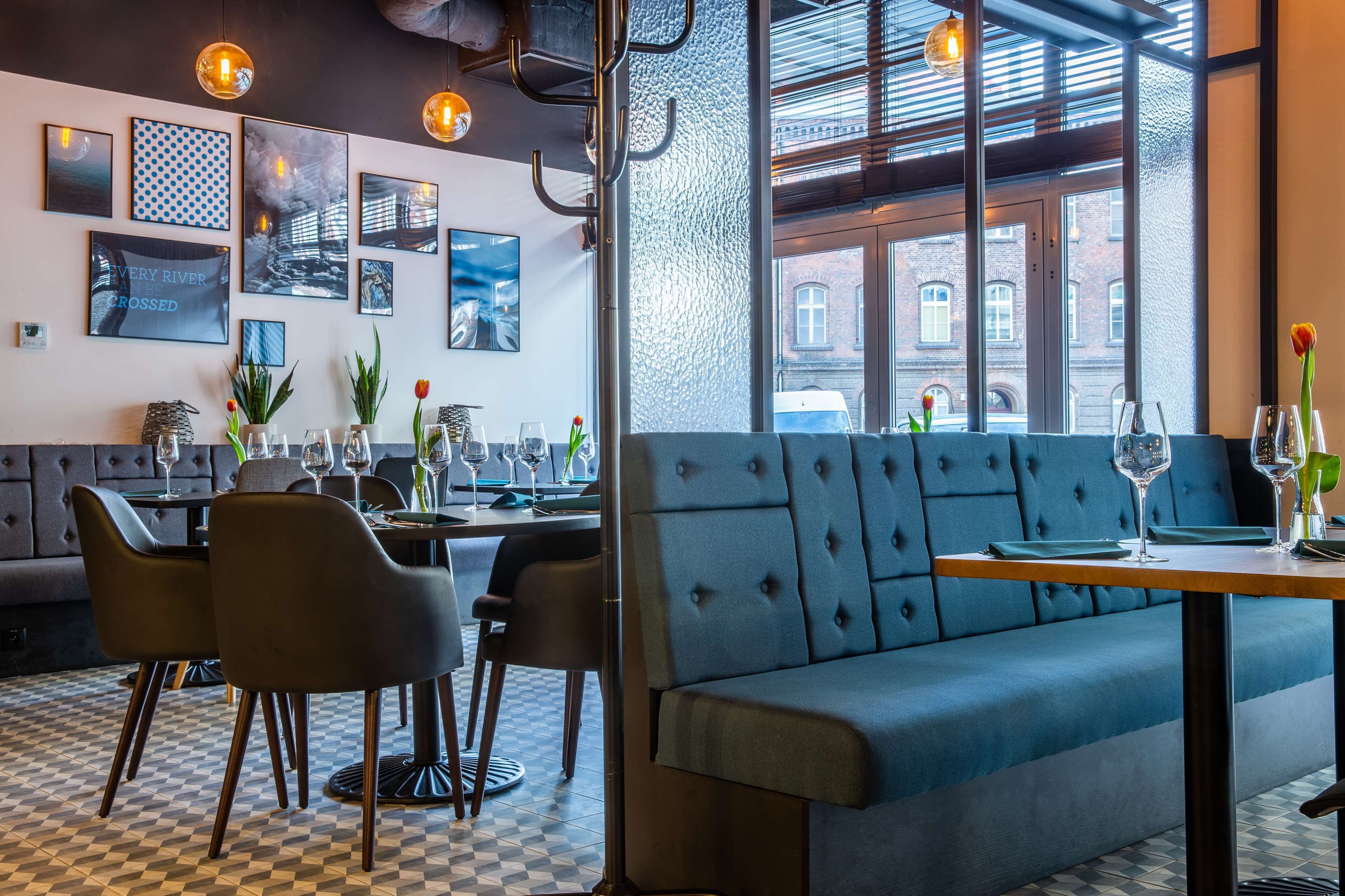 A modern restaurant with a checkered floor, blue upholstered seating, and artwork on the walls.