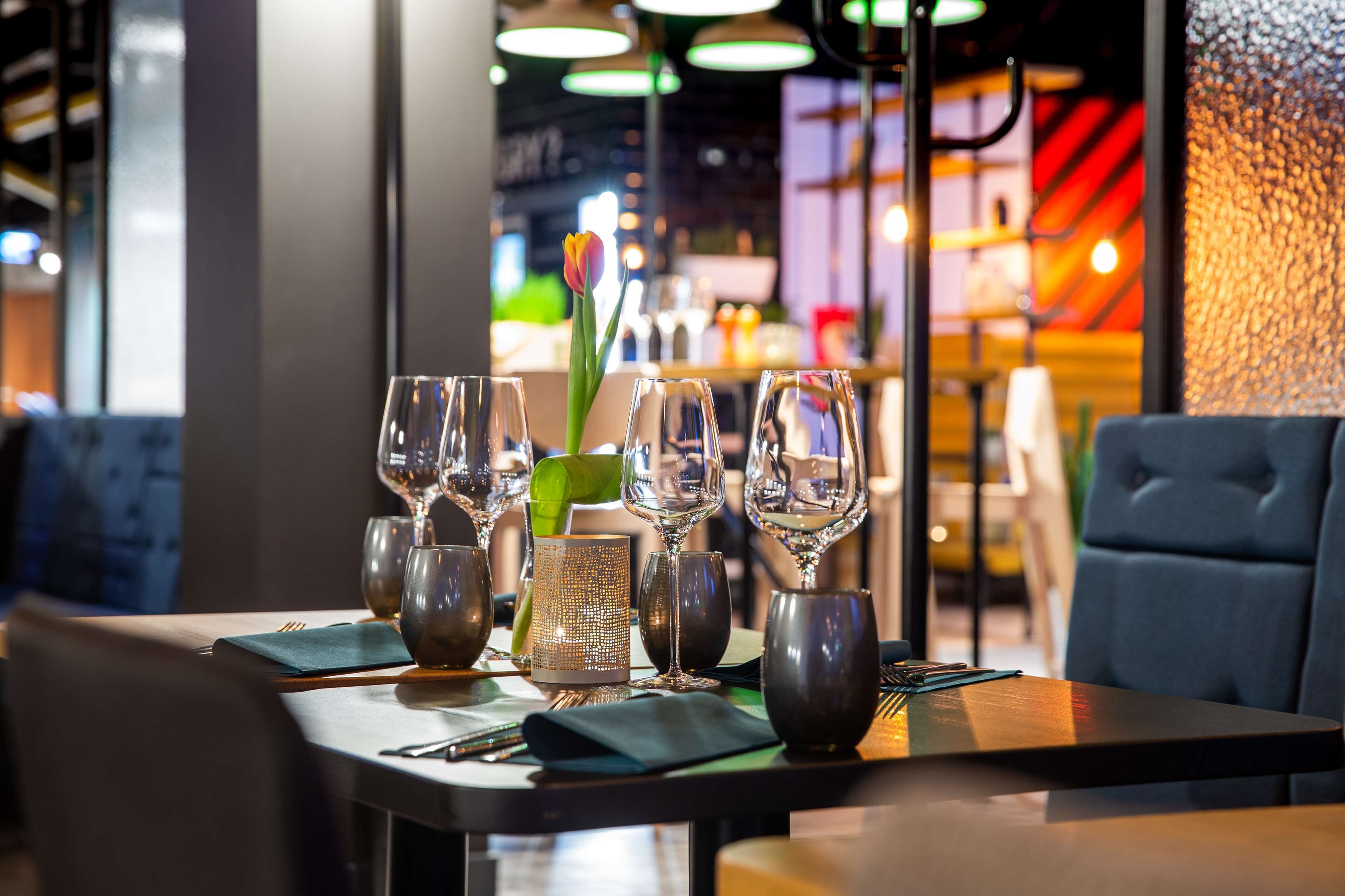 A restaurant table set with wine glasses, a candle holder, and a vase with a flower.