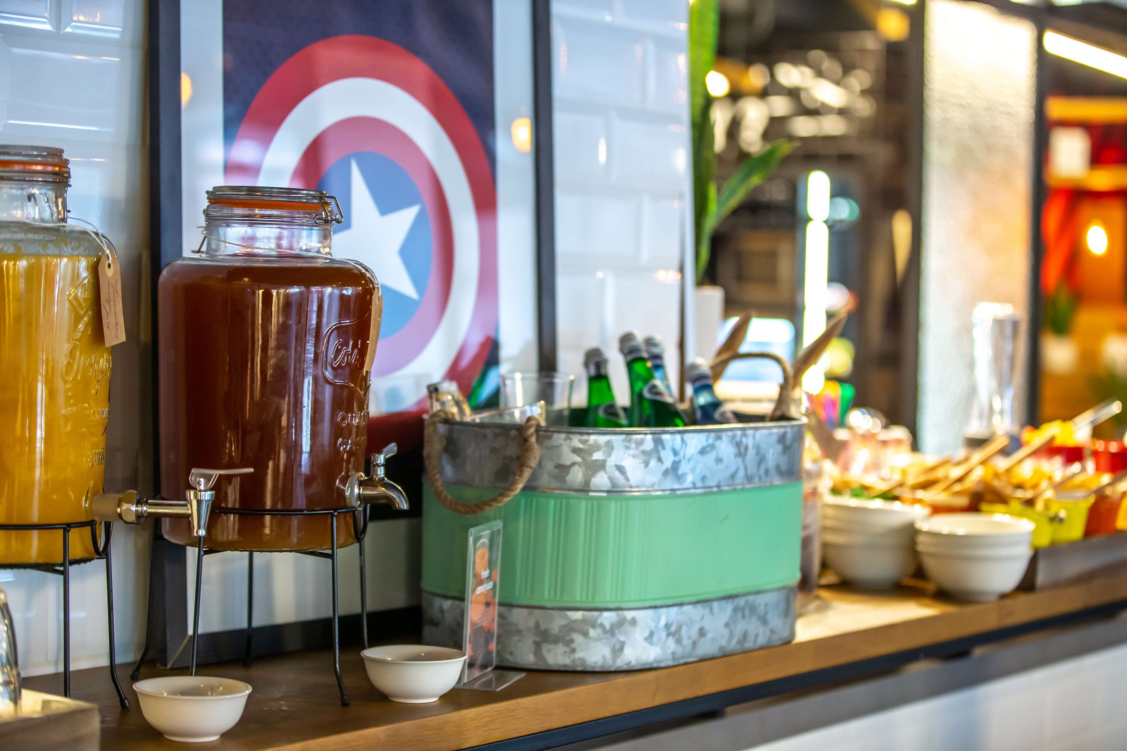 A beverage station with a large pitcher, a smaller pitcher, and a green container with utensils.