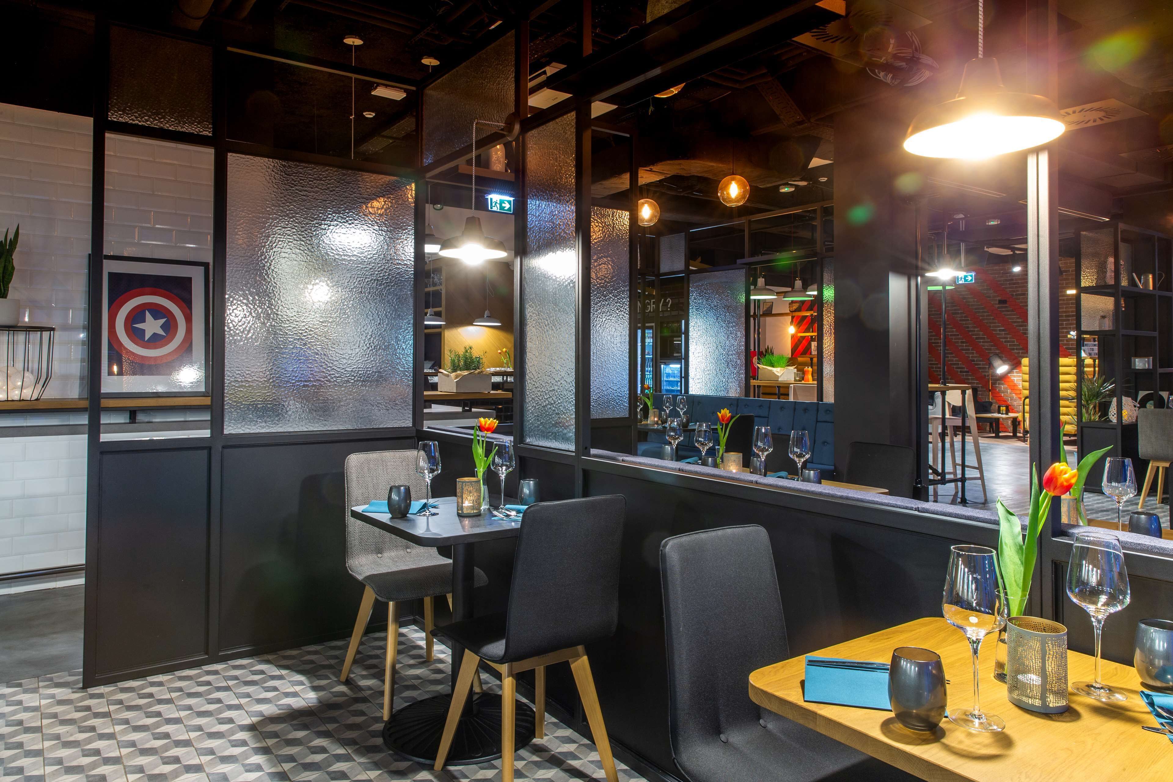 Interior de restaurante con suelo a cuadros, sillas negras y grises, una mesa de madera y un separador de vidrio con un escudo enmarcado de Capitán América.