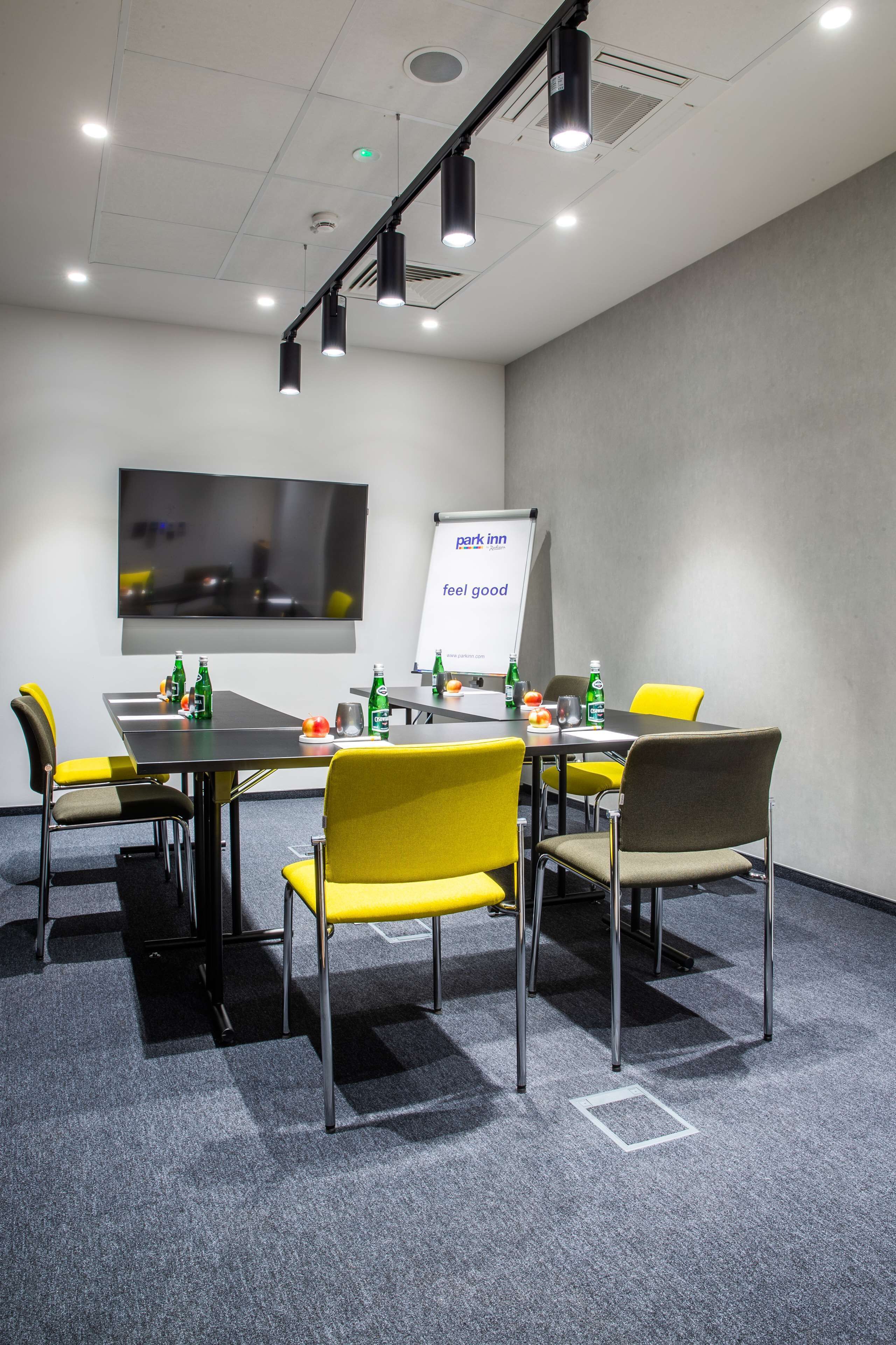 Una sala de conferencias con una gran pantalla plana, una pizarra y una mesa con sillas.